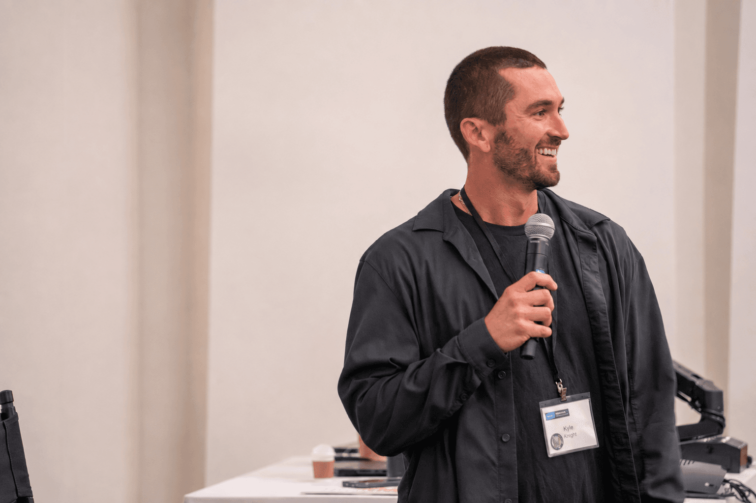 Kyle Knight speaking with a microphone at a UCLA session, his conference badge visible, the room set up behind him